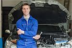 Portrait of confident mechanic leaning aganist car with open hood