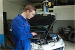 Male mechanic using laptop with car in background