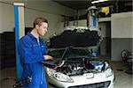 Male repairman using laptop with car in background