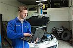 Male mechanic using laptop in garage with car in background