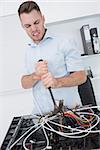 Frustrated young man using hammer to pull out wires from cpu at office