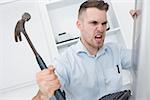 Frustrated young man hitting computer monitor with hammer at office