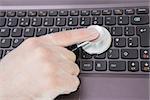 Closeup of hand examining laptop keyboard with stethoscope
