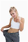 Young healthy woman wearing old pants after losing weight over white background