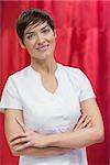 Portrait of a hairdresser with arms crossed against red curtain