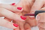 Details shot of hands applying red nail varnish to finger nails at nail salon