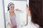 Portrait of young woman brushing her teeth in the mirror