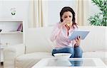 Casual young woman drinking wine while looking at digital tablet on sofa