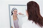 Young woman brushing teeth in bathroom mirror