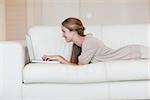 Side view of casual young woman using laptop on sofa at home