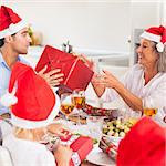 Family exchanging christmas presents around the dinner table wearing santa hats