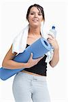 Portrait of young woman in sportswear holding water bottle and mat over white background