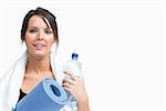 Portrait of young woman holding water bottle and exercise mat over white background