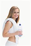Portrait of smiling young woman with towel around neck holding water bottle over white background