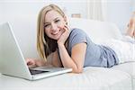 Portrait of casual young woman lying on couch and using laptop at home