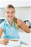 Happy girl eating cereal in kitchen