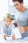 Father pouring milk onto sons cereal at breakfast