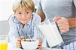 Father pouring milk for sons cereal at breakfast