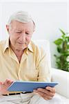 Elderly focused man using a digital tablet on a sofa