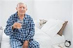 Old man with a water glass sitting on the bed