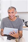 Smiling man using his digital tablet in the kitchen