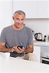 Smiling man touching his smartphone in the kitchen