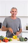 Smiling man cutting a yellow pepper in the kitchen