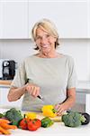 Mature woman cutting a yellow pepper in the kitchen