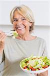 Smiling mature woman eating salad in the kitchen