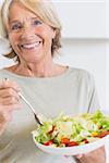 Happy mature woman eating salad in the kitchen