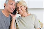 Cheerful mature couple listening a call together in the kitchen