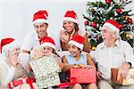 Little girl opening christmas present on couch with family