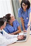 Nurse pointing to something on laptop in meeting with doctor and other nurse