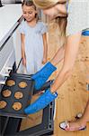 Mother and her daughter taking cookies from the oven in the kitchen