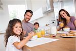 Family smiling at the camera at breakfast in kitchen