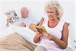 Aged couple reading a book and newspaper on the bed