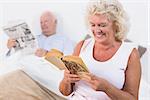 Old couple reading book and newspaper in the bedroom