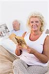 Smiling aged couple reading book and newspaper in the bedroom
