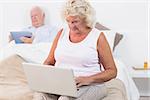 Aged couple using a tablet and the laptop in the bedroom