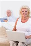 Happy old couple using a tablet and the laptop in the bedroom