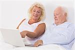 Old couple using a laptop on the bed