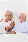 Focused aged couple using a laptop on the bed