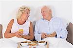 Happy aged couple eating breakfast lying on the bed