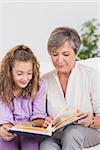 Little girl and her grandmother reading a book in sitting room