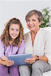 Child and her grandmother looking at the camera with tablet pc in sitting room