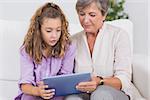 Child and her grandmother holding tablet pc in sitting room