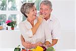 Old man tasting vegetable held by wife in kitchen