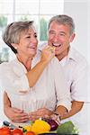 Woman feeding pepper to man in kitchen