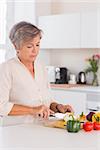 Old woman cutting vegetables on a cutting board in kitchen