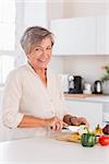 Old woman cutting vegetables on a cutting board with a smile in kitchen